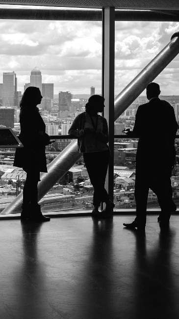 A group of people having a conversation in an office building overlooking Canary Wharf in London, UK 